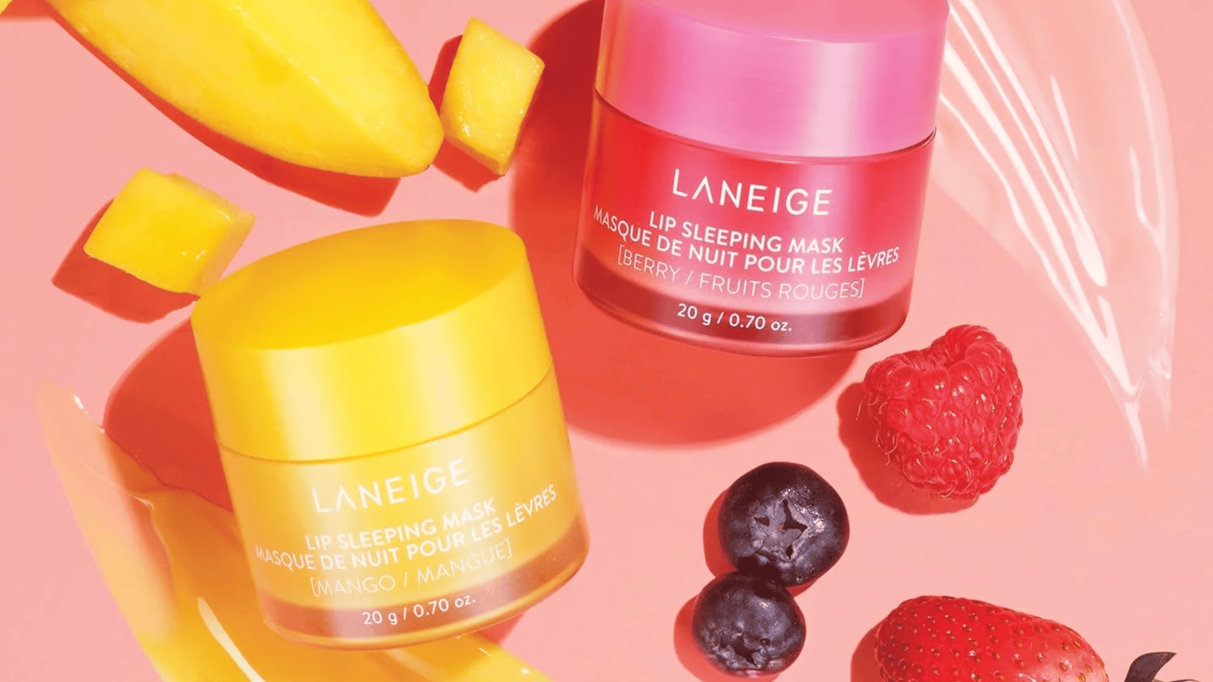 Bilden visar Laneige Lip Sleeping Mask i mango och bärsmaker, omgivna av färska frukter som mango, hallon och blåbär. Produkterna framstår som fuktgivande och näringsrika för läpparna, perfekta för nattvård.