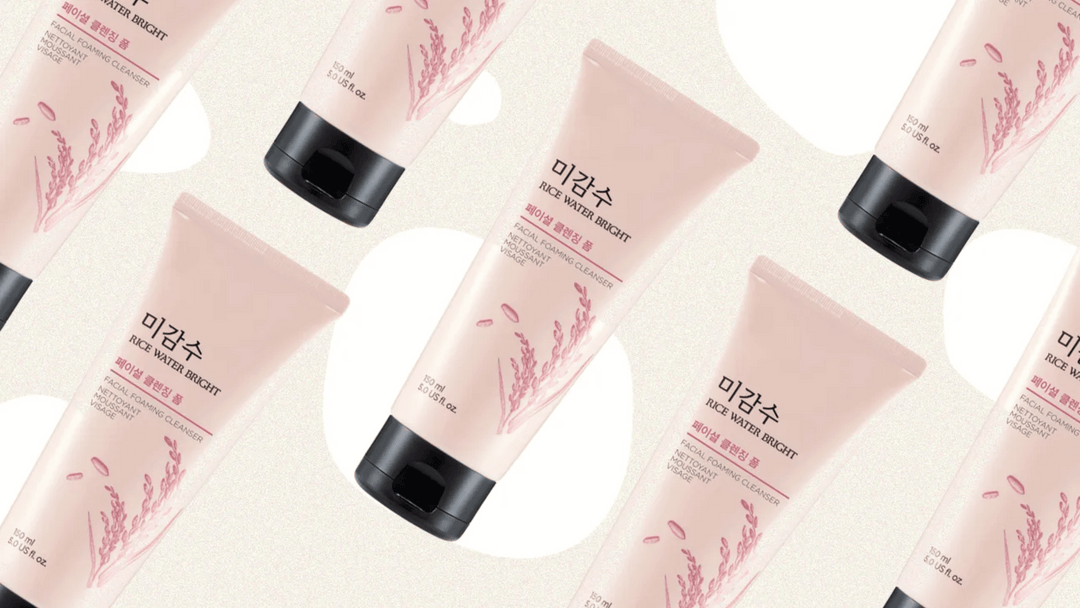 Ljusrosa tuber av "RICE WATER BRIGHT FACIAL FOAMING CLEANSER" med risplant illustrationer.