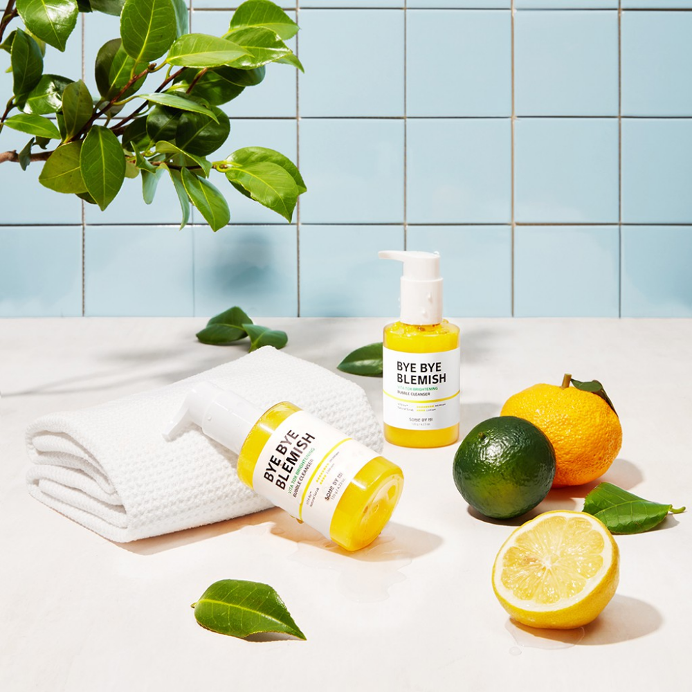 Ett bord med Bye Bye Blemish Vita Tox Brightening Bubble Cleanser 120g från Some By Mi, citroner och limefrukter.